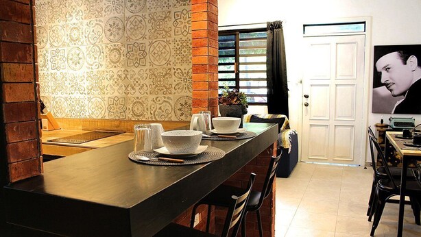 Une cuisine avec un long comptoir en bois, un dosseret décoré et une porte ornée d’une affiche.