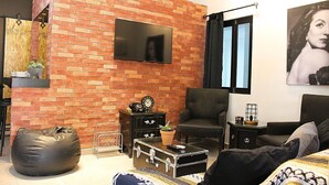 Un salon avec un mur en briques, un téléviseur à écran plat, un fauteuil confortable, un canapé et une table basse.
