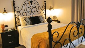 Un lit bien fait, avec une couette blanche et un plaid marron, une tête de lit en métal noir et deux lampes de chevet.