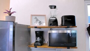 Een keuken met een koelkast, een koffiezetapparaat, een blender, een magnetron en een lijstje in een kast.