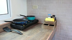 Een keuken met een gasfornuis, twee koekenpannen, een spatel en een houten kruidenrek met potjes.