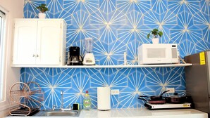 Une cuisine avec un revêtement mural bleu à motifs géométriques, des meubles blancs, un four à micro-ondes, un mixeur et une cuisinière.