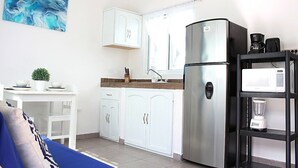 Une cuisine de taille réduite avec des meubles blancs, un réfrigérateur en acier inoxydable, un four à micro-ondes et une machine à café.