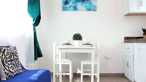 Une pièce avec une table blanche, deux chaises, une plante en pot et un tableau accroché au mur.