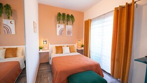 Una habitación de hotel con dos camas, un banco verde, una ventana con cortinas naranjas y una obra de arte en la pared.