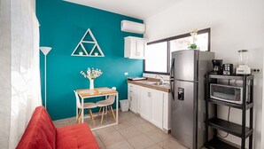 Cocina compacta con una pared de acento color turquesa, armarios blancos, un refrigerador de acero inoxidable, un microondas y una cafetera.