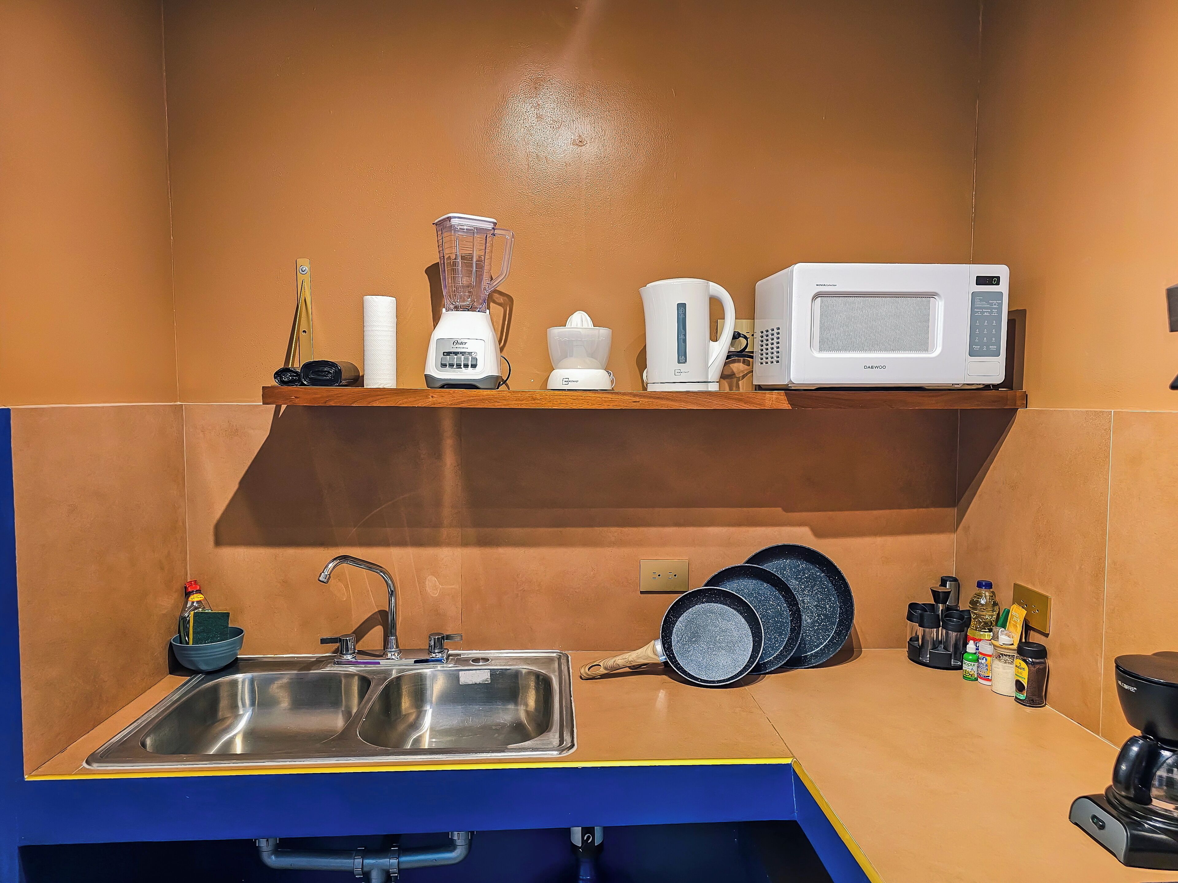 A kitchen with a sink, a microwave, a blender, and a kettle on a shelf.