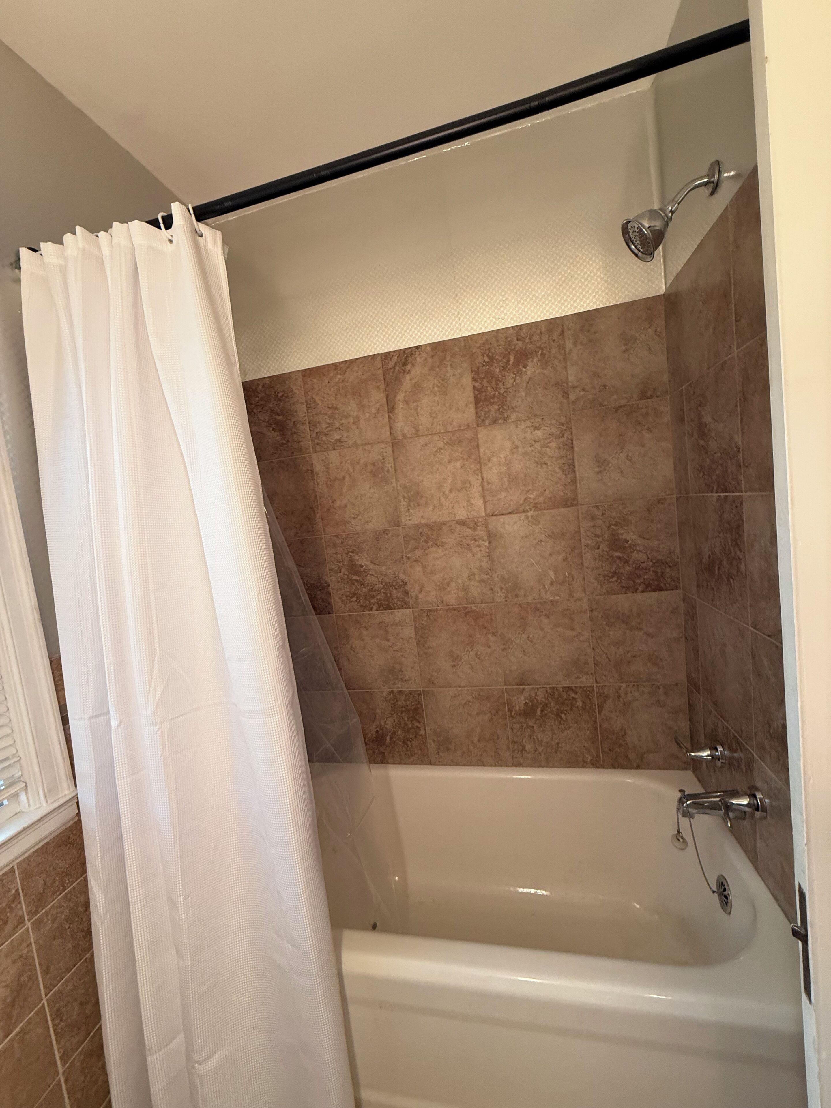 Une salle de bain avec une baignoire, des carreaux de couleur beige et un rideau de douche blanc.