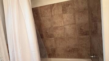 Une salle de bain avec une baignoire, des carreaux de couleur beige et un rideau de douche blanc.