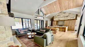 Amplia sala de estar con techo alto, chimenea de piedra y cocina con armarios de madera.