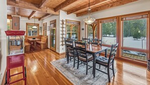A wooden interior with a dining table and chairs, large windows, and a kitchen area with a red appliance.