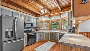 A kitchen with wooden beams, a stainless steel refrigerator, a stove, and a large window.