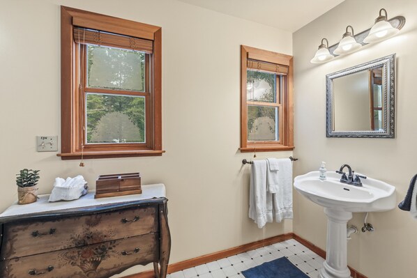A bathroom with a wooden vanity, a white sink, and two windows with wooden frames.