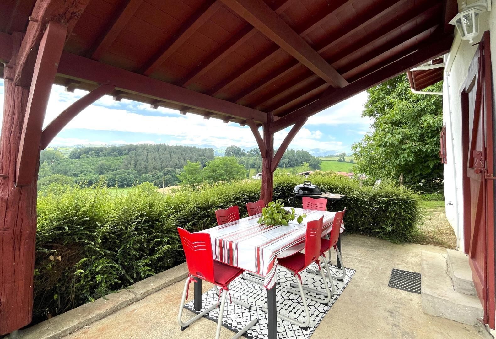 An outdoor dining area with a table and chairs, a grill, and a view of the countryside.