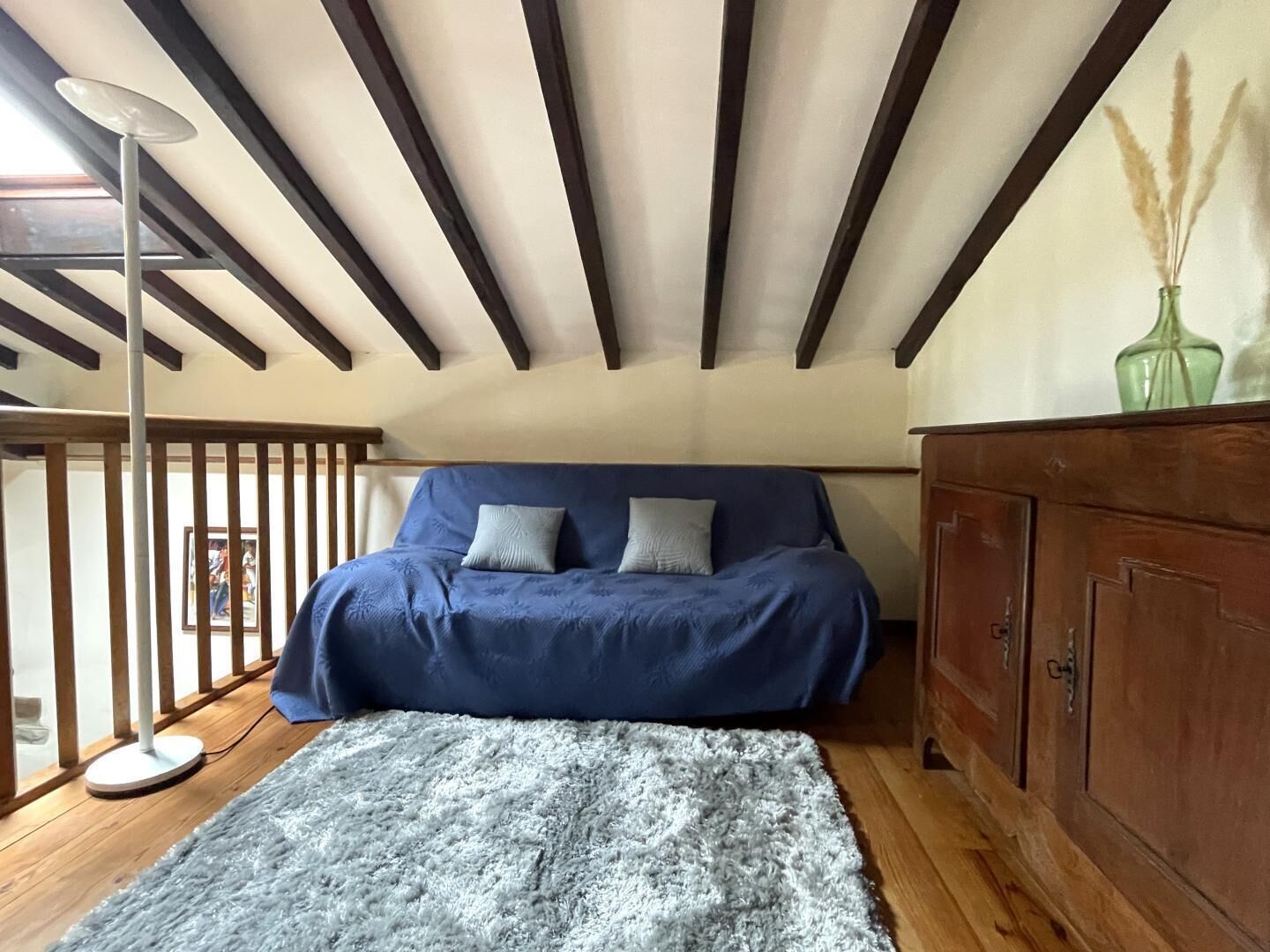 Ein Schlafzimmer mit einem blauen Bett, einem grauen Teppich, Holzböden, einem Holzschrank und einer Decke mit freiliegenden Balken.
