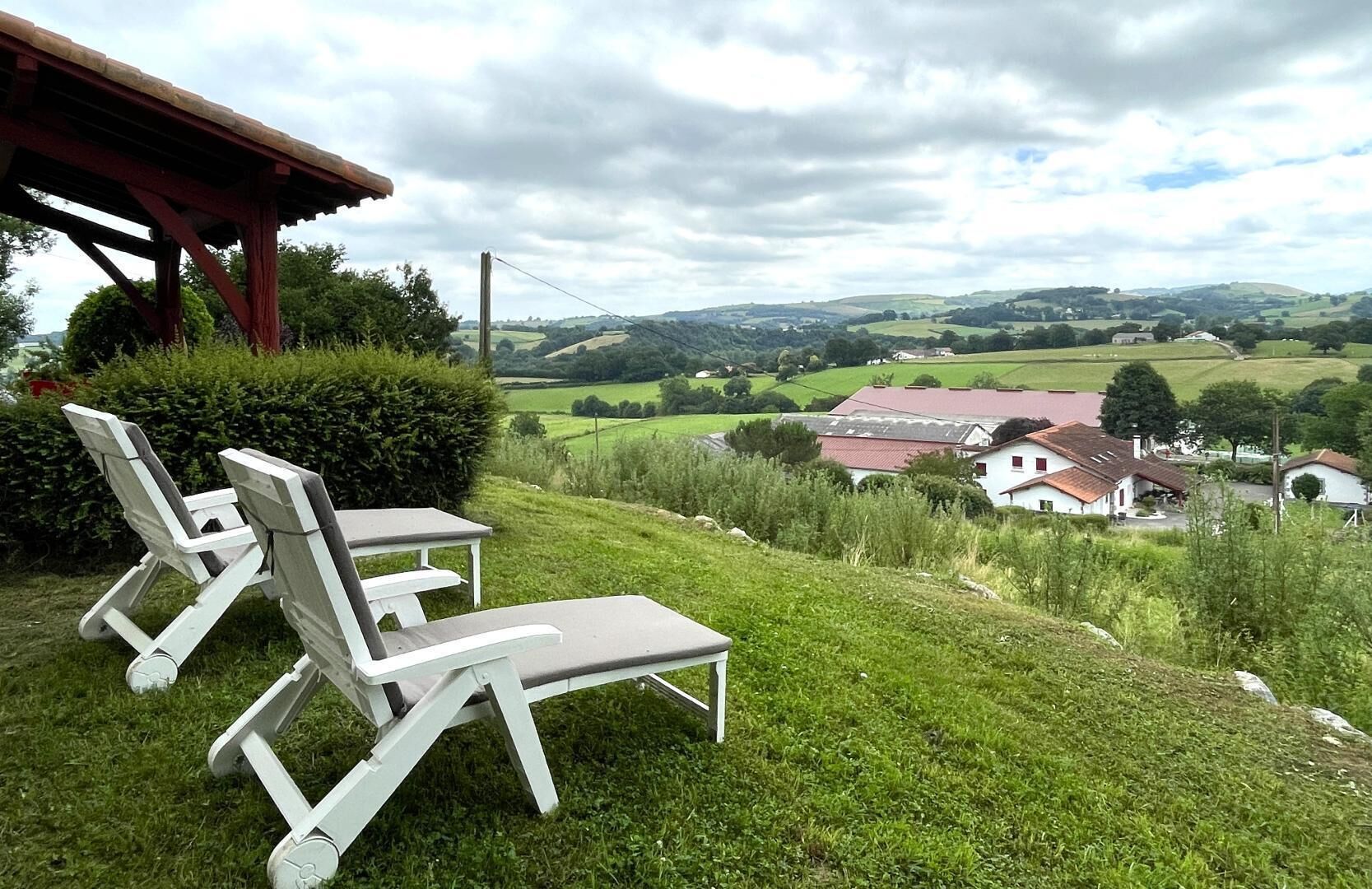 Un espace extérieur verdoyant, avec des chaises longues blanches et, au fond, un bâtiment surmonté d’un toit rouge.