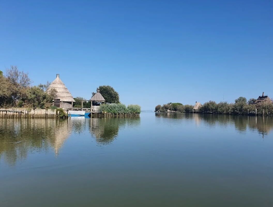 A calm lake with a traditional thatched-roof hut and a small boat docked on the shore.