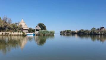 A calm lake with a traditional thatched-roof hut and a small boat docked on the shore.