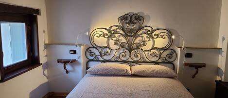 Un dormitorio con una cama, dos mesitas de noche, una ventana y un cabecero decorativo de metal.
