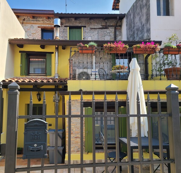 A yellow building with a balcony, a metal gate, and outdoor seating.