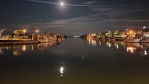 Una marina nocturna con barcos amarrados, agua tranquila que refleja luces y un cielo despejado.