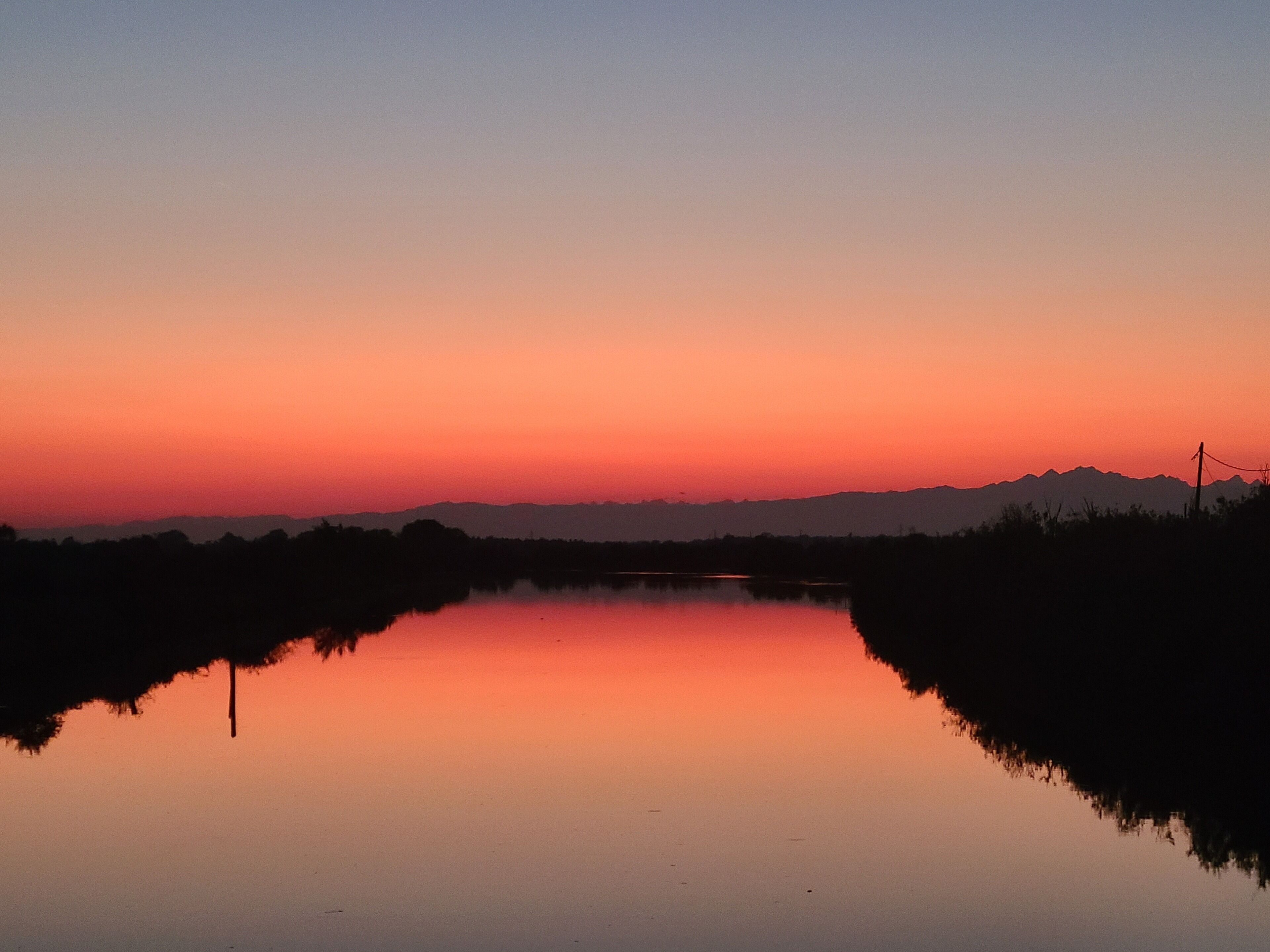 Um lago calmo ao pôr do sol, com montanhas ao fundo.