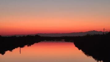 Um lago calmo ao pôr do sol, com montanhas ao fundo.
