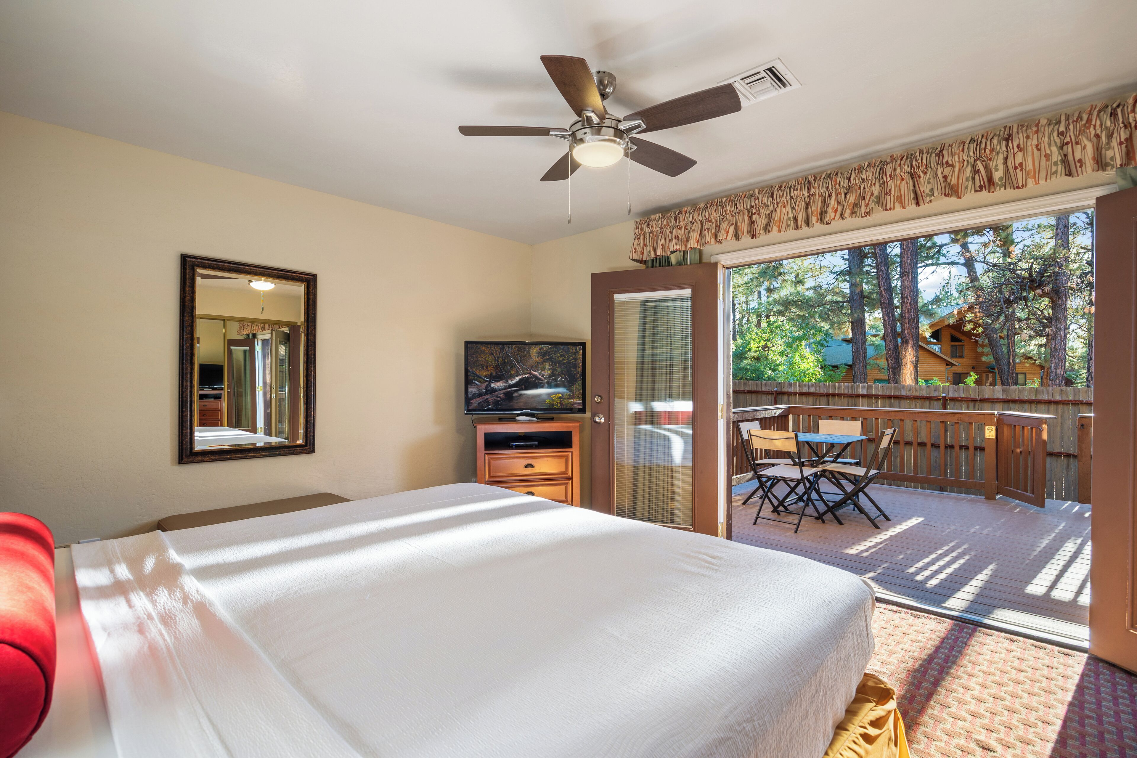 Une chambre avec un lit, un ventilateur de plafond, une télévision et un balcon donnant sur la verdure.
