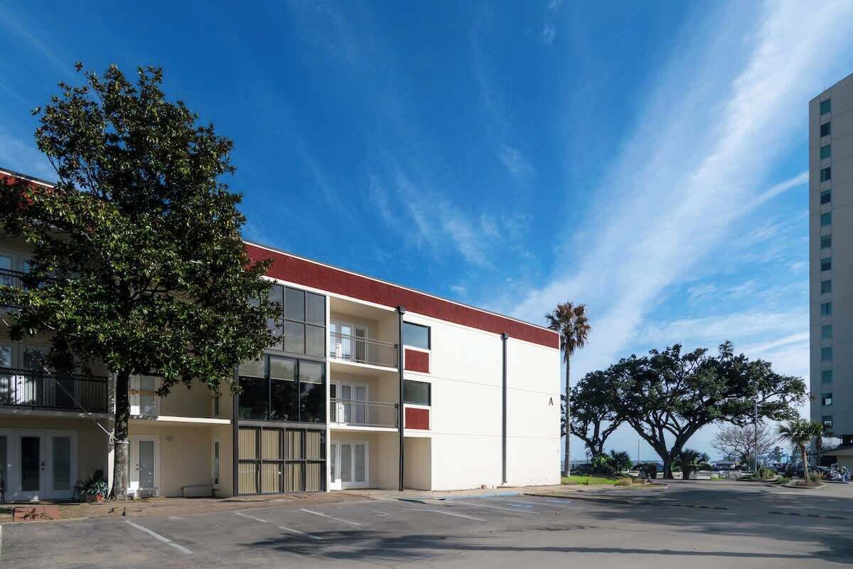 Un edificio de varios pisos con techo plano, ventanas amplias y un estacionamiento al frente.