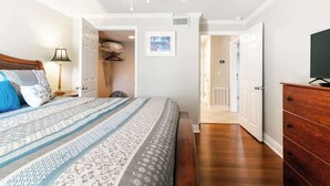 Une chambre à coucher comprenant un lit, un ventilateur de plafond, une commode et une porte donnant sur une autre pièce.