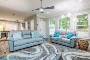 A living room with two sofas, a patterned rug, a ceiling fan, and large windows. - Legacy Villa 2602 - 3 Bedroom 2 Bath With Garage in Beachside Neighborhood (Gulfport)