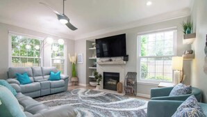 A living room with a gray sofa, teal armchairs, a patterned rug, a fireplace, and a TV mounted above it. - Legacy Villa 2602 - 3 Bedroom 2 Bath With Garage in Beachside Neighborhood (Gulfport)