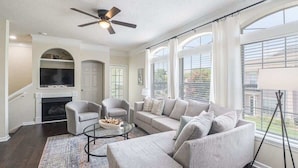 A living room with a fireplace, sofa, armchairs, and a ceiling fan. - Legacy Villa 203 - 2 Bedroom 2 Bath With Garage in a Beachside Neighborhood (Gulfport)