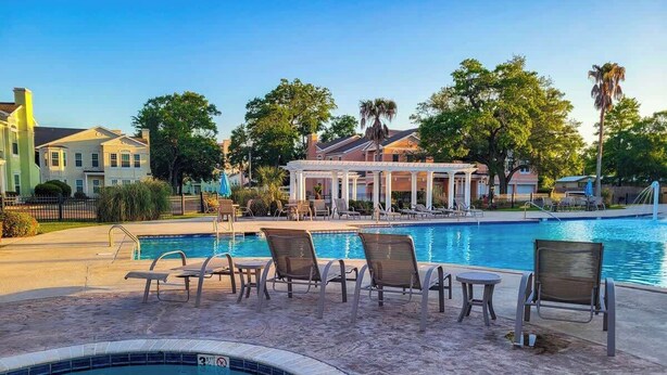A pool area with lounge chairs, a covered seating area, and a view of surrounding buildings. - Legacy Villa 1103 - 1 Bedroom 1 Bath With Garage in Beachside Neighborhood (Gulfport)