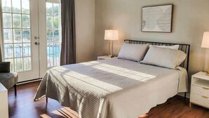 A bedroom with a large bed, a nightstand, a chair, and a view of a pool through a glass door. - Legacy Villa 1103 - 1 Bedroom 1 Bath With Garage in Beachside Neighborhood (Gulfport)