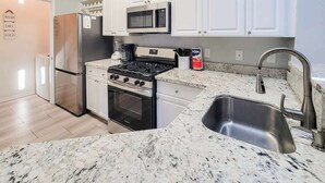 A kitchen with white cabinets, stainless steel appliances, a granite countertop, and a sink. - Legacy Villa 1103 - 1 Bedroom 1 Bath With Garage in Beachside Neighborhood (Gulfport)
