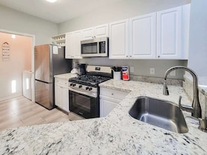 A kitchen with white cabinets, stainless steel appliances, a granite countertop, and a stainless steel sink. - Legacy Villa 1103 - 1 Bedroom 1 Bath With Garage in Beachside Neighborhood (Gulfport)