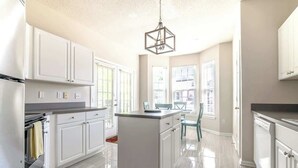 A modern kitchen with white cabinets, a central island, and a hanging light fixture.