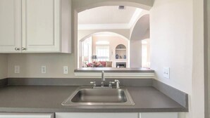 A kitchen with a stainless steel sink, white cabinets, and a view into the living area through an archway.