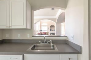 A kitchen with a stainless steel sink, white cabinets, and an arched doorway leading to a living area. - Legacy Villa 506 - 2 Bedroom 2 Bath With Garage in Beachside Neighborhood (Gulfport)