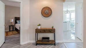 A hallway with a wooden console table, a decorative wall piece, and a view into a kitchen area.
