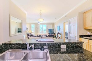 A kitchen with granite countertops, stainless steel sinks, and a dining area with a table and chairs. - Beachview Condo at Legacy Tower 1 -202 - Fully Furnished 2 Bedroom 2 Bathroom (Gulfport)