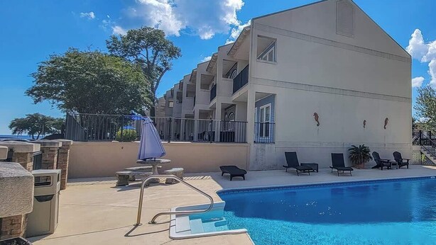 A poolside area with a clear blue pool, lounge chairs, and a building with balconies. - Creole Coast (Long Beach)