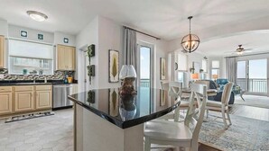 A modern kitchen with a central island, dining area with chairs, and a view to the outside. - The Cobalt View (Gulfport)