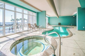 A pool area with two hot tubs, a seating area with chairs, and large windows offering a view of the beach. - Blue Water Suite (Gulfport)