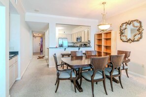 A dining area with a table and chairs, a kitchen in the background, and a decorative mirror on the wall. - Beachview Condo in Legacy Tower 1 -1104 - Fully Furnished 2 Bedroom 2 Bath (Gulfport)