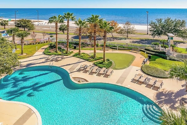 A swimming pool with lounge chairs, palm trees, and a view of the beach. - Beachview Condo in Legacy Tower 1 -1104 - Fully Furnished 2 Bedroom 2 Bath (Gulfport)
