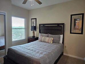 A bedroom with a bed, a nightstand, a window with blinds, and a ceiling fan. - Beachview Condo at Legacy Tower 2 -708 - Fully Furnished 2 Bedroom 2 Bathroom (Gulfport)