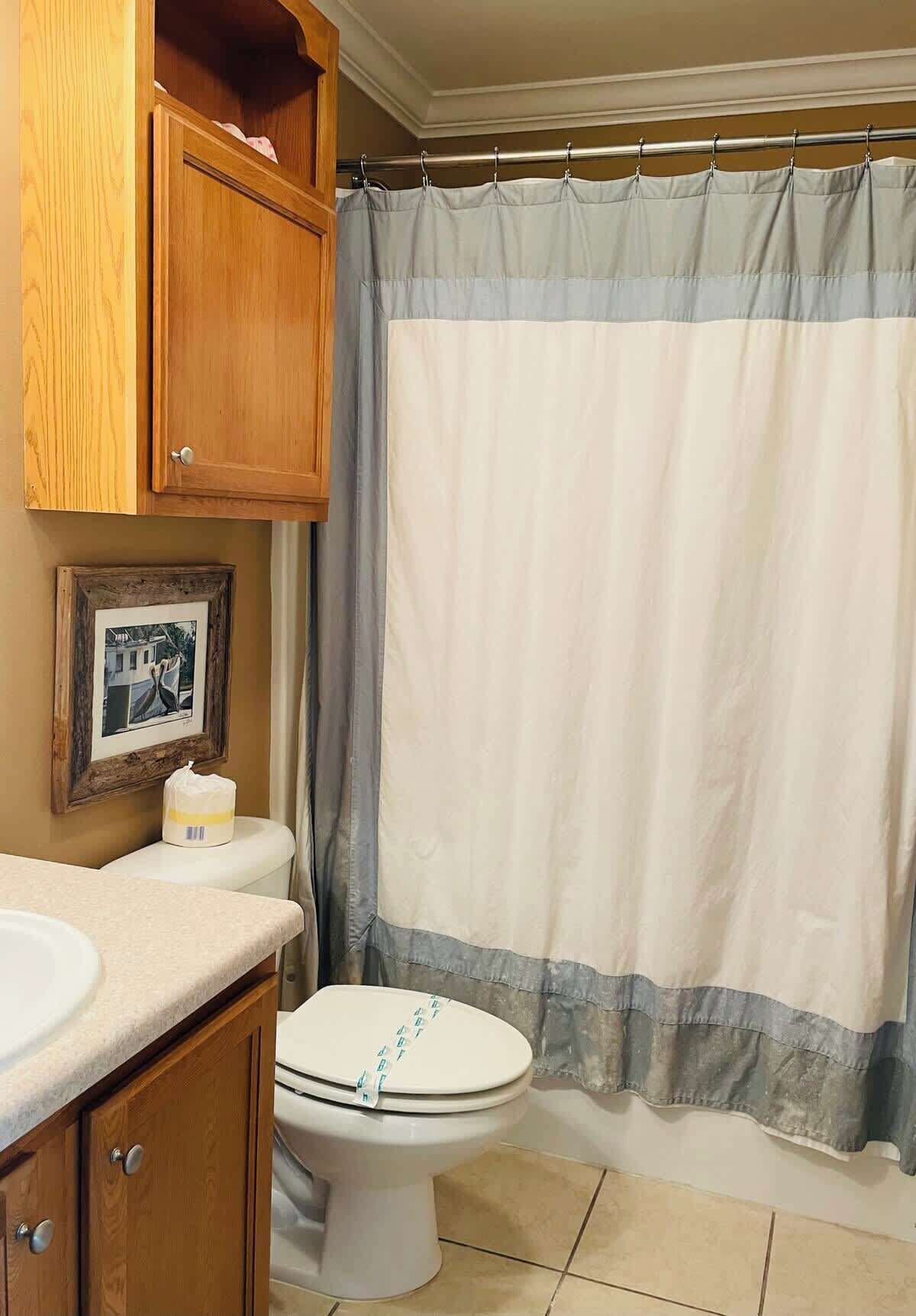 Une salle de bain avec un meuble en bois, des toilettes, un tableau encadré et un rideau de douche.