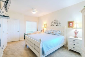 A bedroom with a white bed, bedside tables, a door, and a window with blinds.